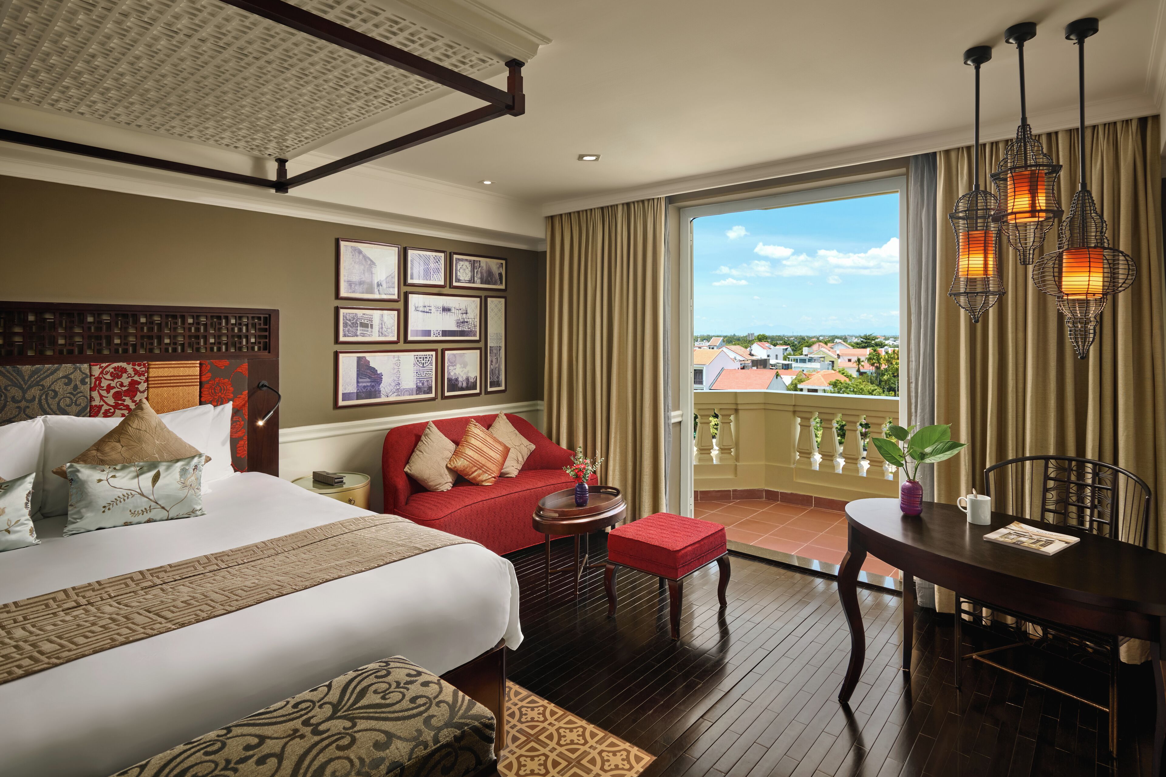 Habitación de hotel con una cama grande, un sofá rojo, una mesa de comedor y un balcón con vistas a edificios.