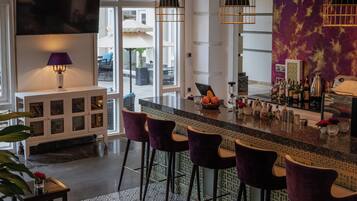 A bar area with a patterned floor, bar stools, a television, and a large window with blinds.
