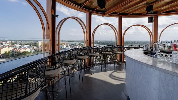 Un bar en un rascacielos con vistas panorámicas de la ciudad, que presenta vigas de madera curvas y sillas de metal.