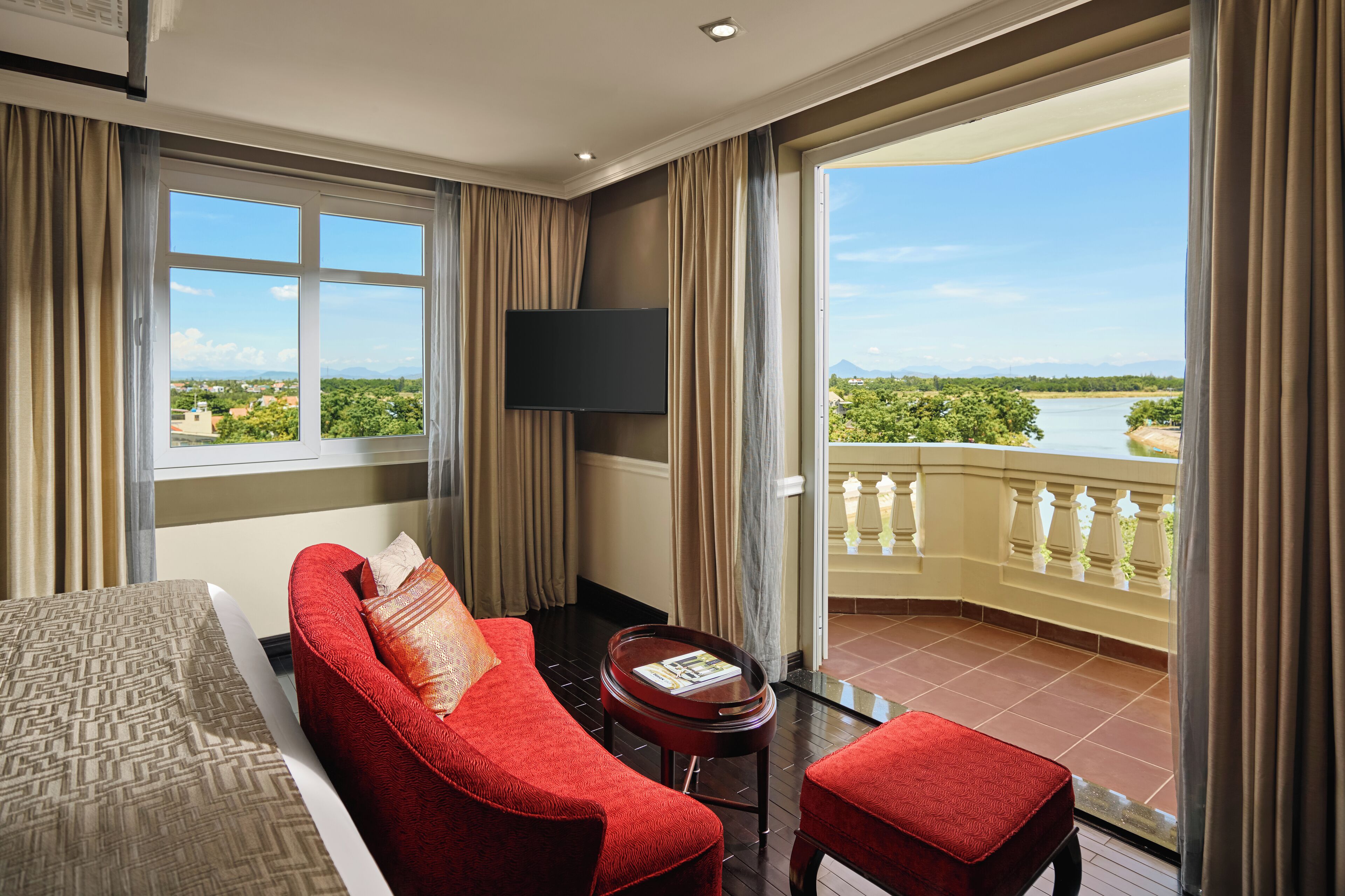 Une chambre d’hôtel dotée d’un grand balcon, d’un canapé rouge, d’une petite table ronde et d’un téléviseur fixé au mur.