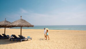 Una playa con sillones de playa y sombrillas de paja.