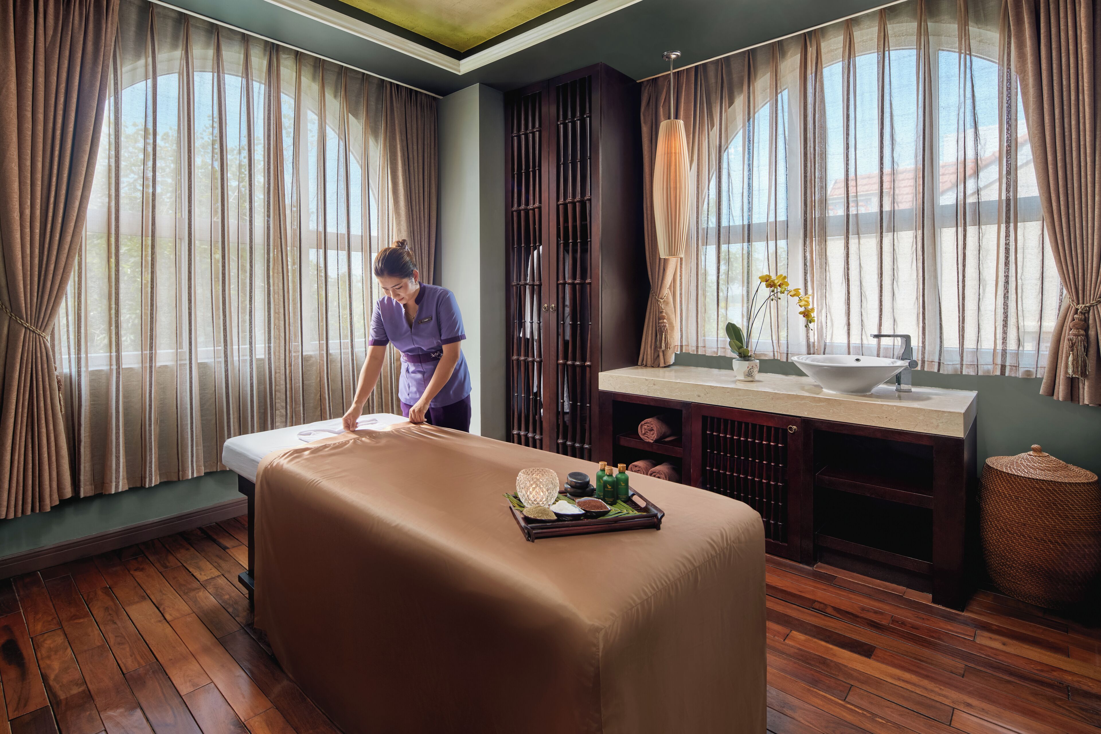A massage room with a massage table, a tray with massage oils, and a window with curtains.