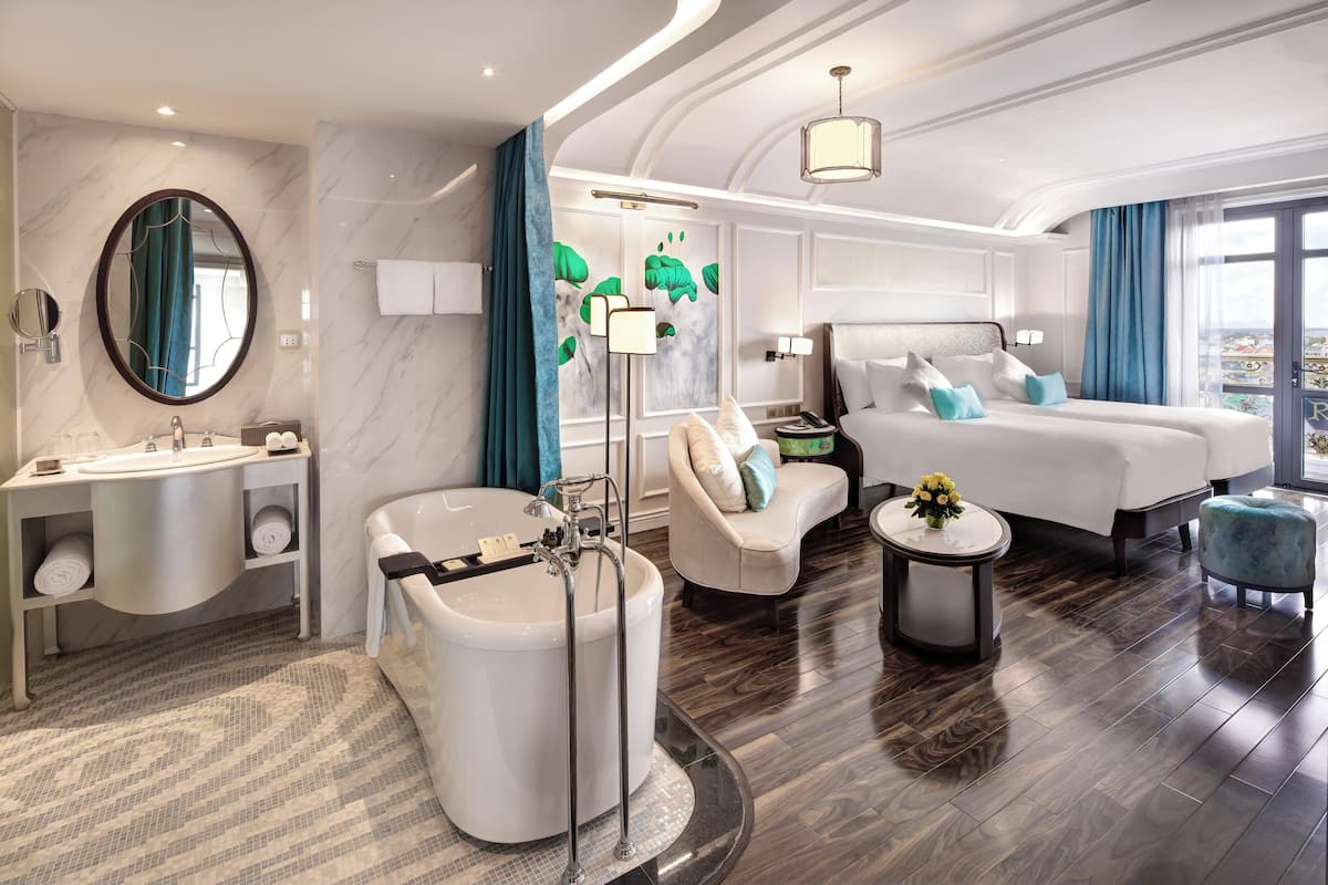 Habitación de hotel moderna con una cama grande, un área de descanso, un baño con bañera y vistas a la ciudad.