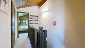 Um corredor com teto de madeira, uma placa com nomes de quartos, uma placa com o número 14 e uma porta que dá para um quarto com uma cama.