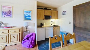 Cozinha compacta com armários de madeira, micro-ondas e pia. Possui área de refeições com mesa e cadeiras.