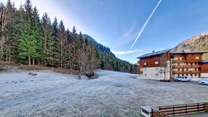 Ein Gebäude mit einer Holzfassade und mehreren Balkonen, umgeben von bewaldeter Landschaft und blauem Himmel.