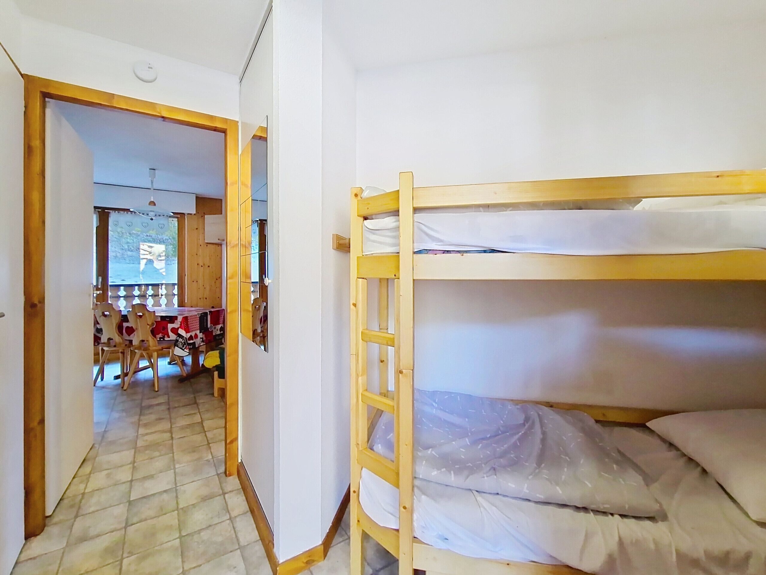 Une chambre avec des lits superposés, une porte en bois et une vue sur un espace extérieur aménagé avec une table et des chaises.