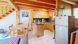 A cozy cabin-style kitchen with wooden cabinets, a dining area with a table and chairs, and a built-in island with a refrigerator and microwave. - Chalet Papillon PPL NATURE & COSY 6 Pers. (Châtel)