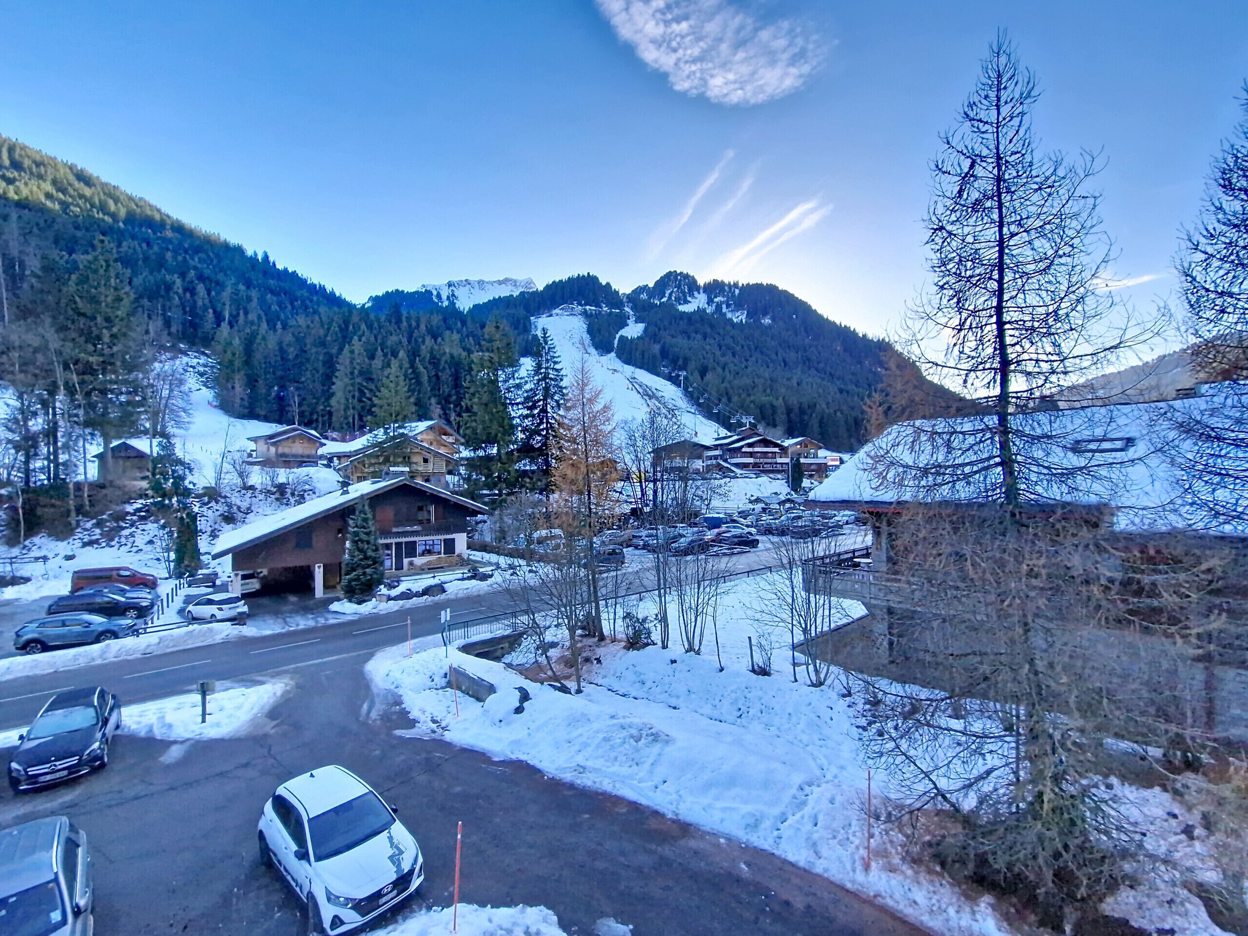 A snow-covered mountain village with buildings, a road, and parked cars.