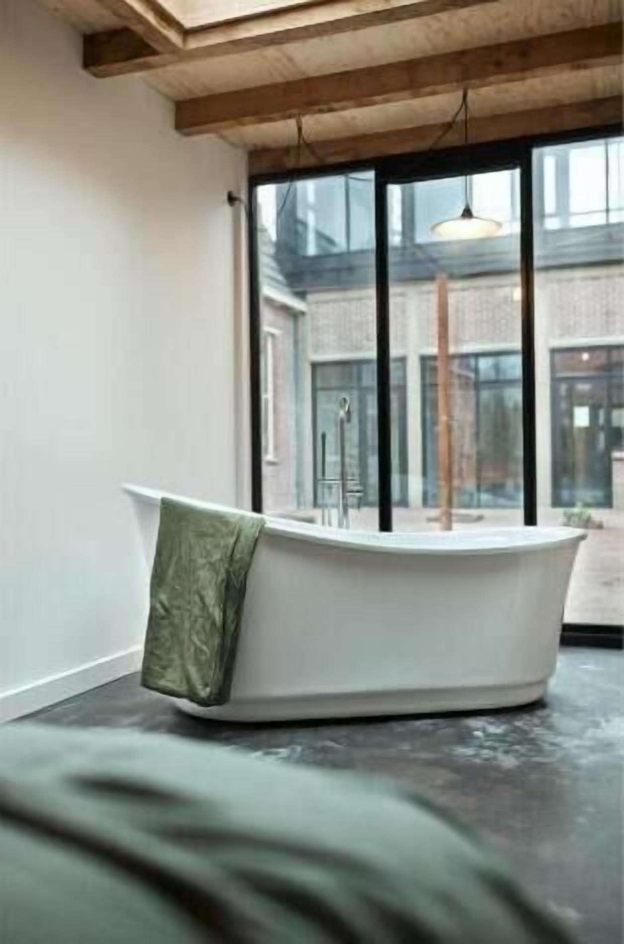 A modern bathroom with a freestanding bathtub, large windows, and a visible outdoor courtyard.