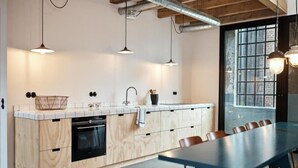 Een moderne keuken met houten kastjes, een zwarte oven en een blauwe eettafel met stoelen.