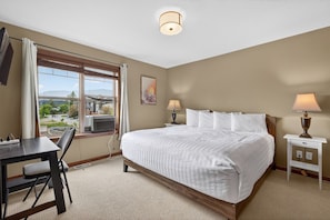 A hotel room with a large bed, a desk, a chair, a window with a view, and a lamp. - 3 BDR Townhouse / Pet friendly / Great Location (Invermere)