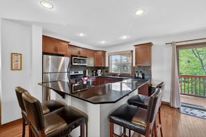 A kitchen with a central island, wooden cabinets, stainless steel appliances, and a balcony with a view.