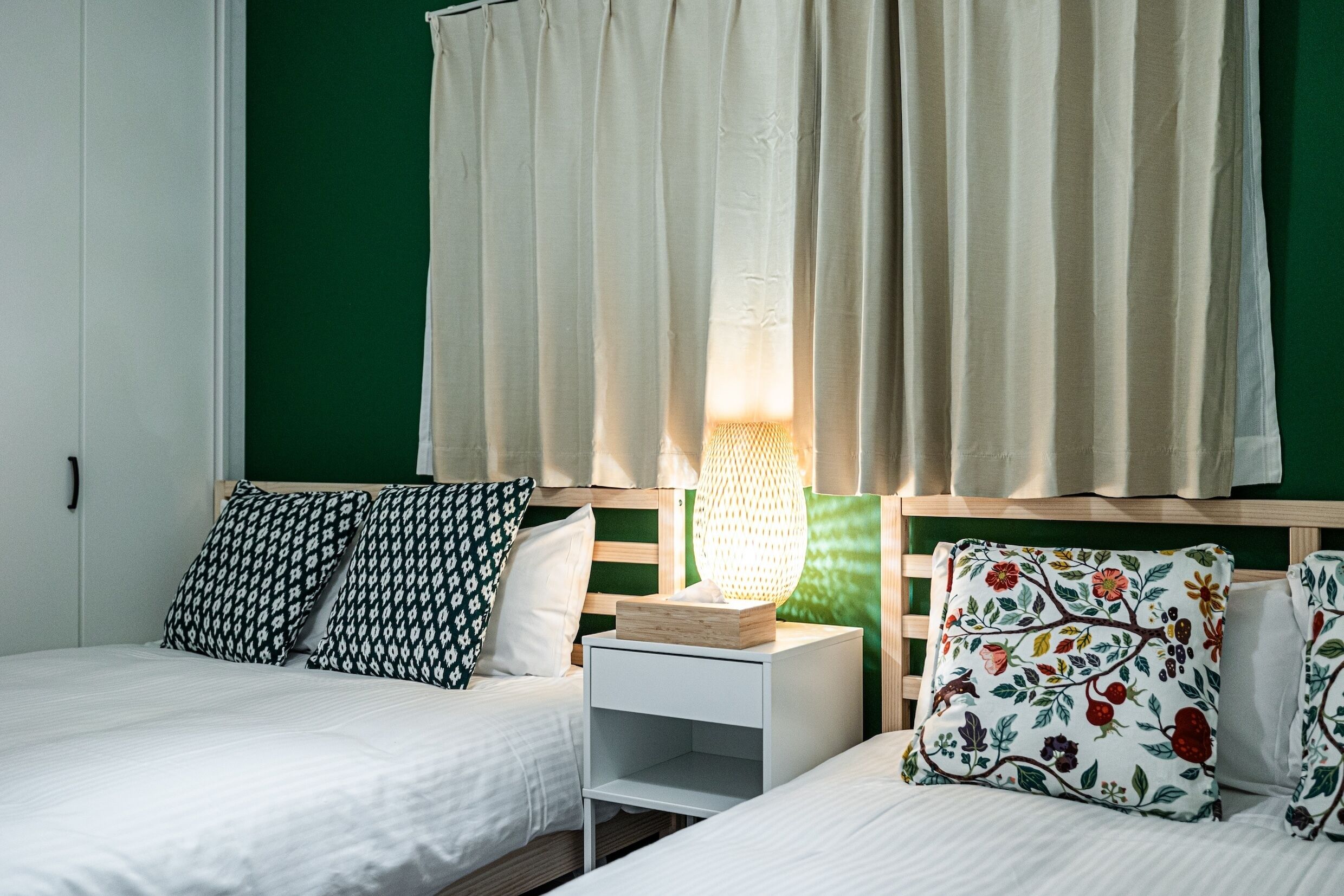 A bedroom with two beds, a nightstand, a lamp, and a green wall.