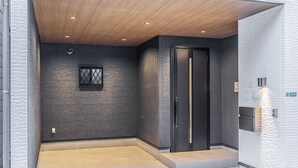 Un espace d’ascenseur moderne avec un mur texturé, un plafond en bois et une porte dotée d’une bande lumineuse verticale.