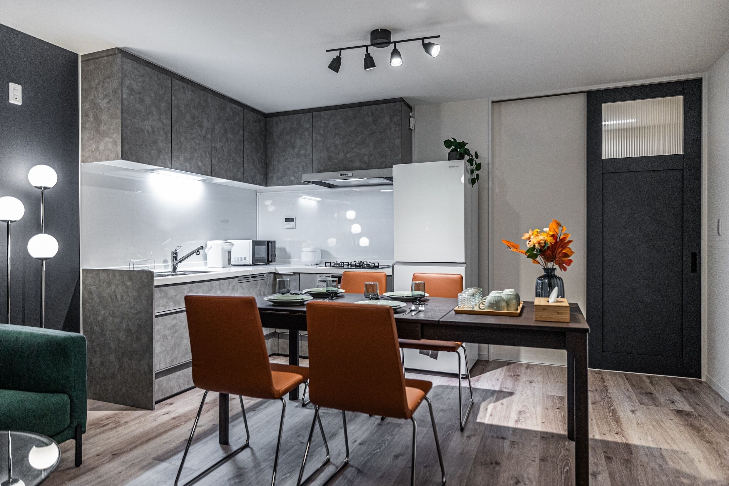 A modern kitchen with a dining area, featuring a central island, dark cabinetry, and a vase with flowers on the table.