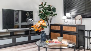 Un salon moderne avec un téléviseur à écran plat, une table basse en verre, un vase avec des fleurs, un magazine et un meuble noir et blanc.