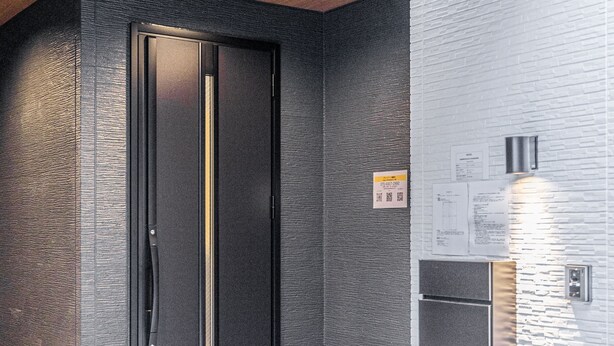 Un ascenseur moderne avec une porte noire et des poignées métalliques, situé à côté d’un mur texturé agrémenté d’un luminaire.