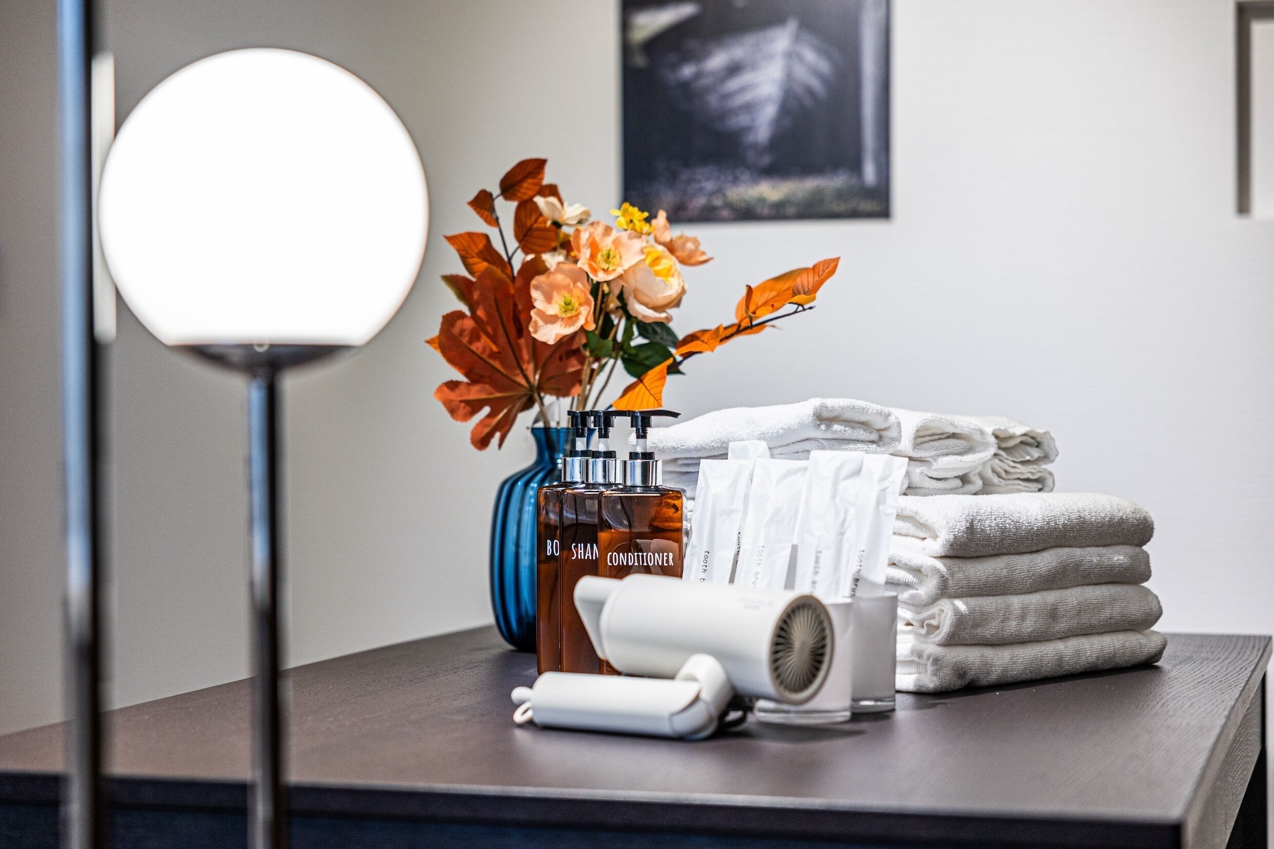 A bathroom vanity with a bottle of conditioner, a hairdryer, and a vase of flowers.