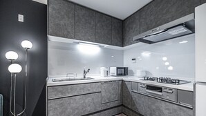 Une cuisine moderne avec des meubles gris, un plan de travail blanc, une cuisinière à gaz, un four à micro-ondes et un évier.