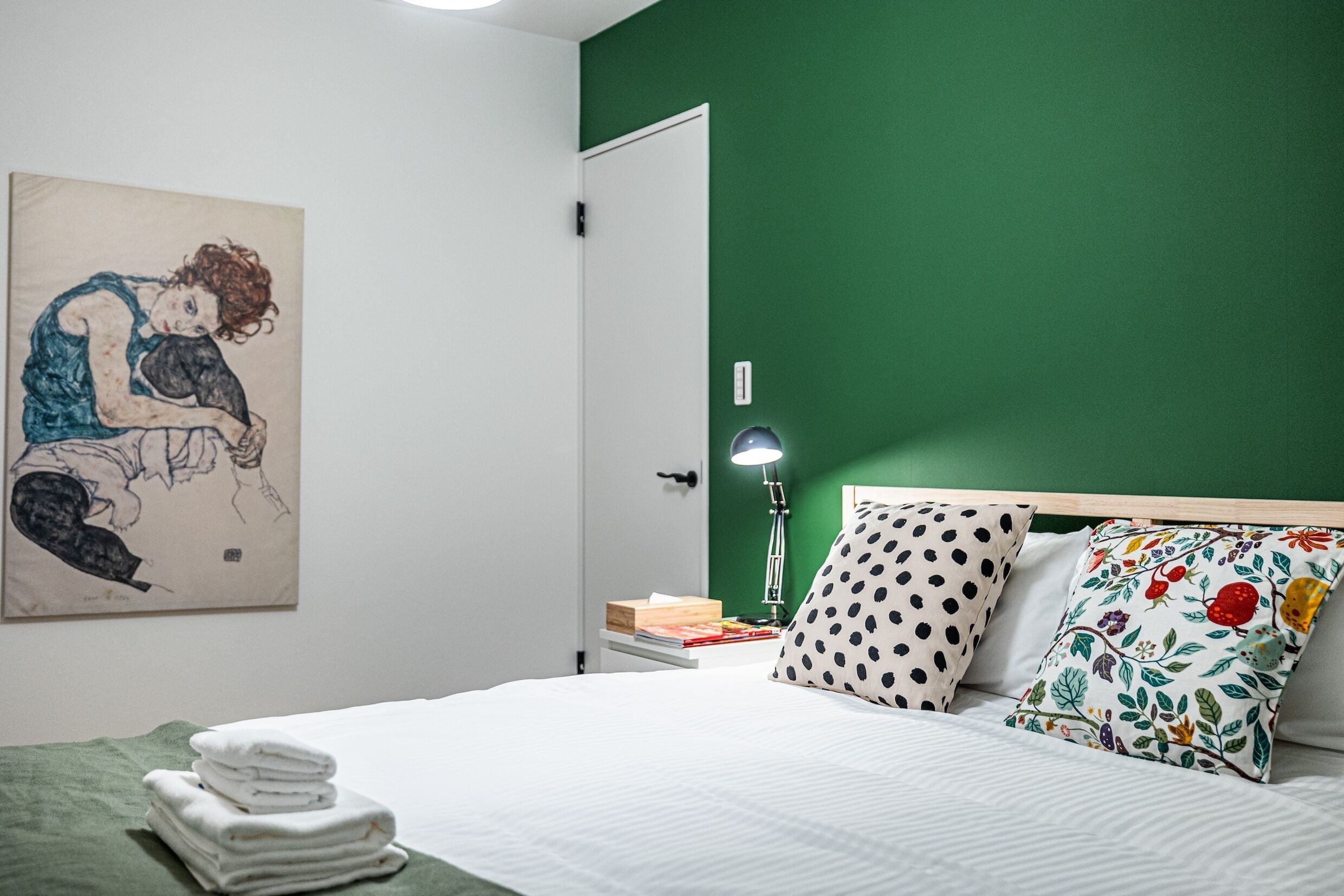 Una cama bien hecha con ropa blanca, una pared verde y un cuadro de una mujer.