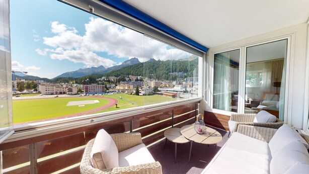 A balcony with wicker furniture, a view of a sports field, and a mountainous landscape. - Well-kept holiday apartament house in a prime location in St. (St. Moritz)