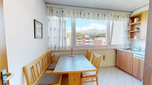 A small kitchen with a dining area, wooden cabinets, and a window with a view of buildings and mountains. - Well-kept holiday apartament house in a prime location in St. (St. Moritz)
