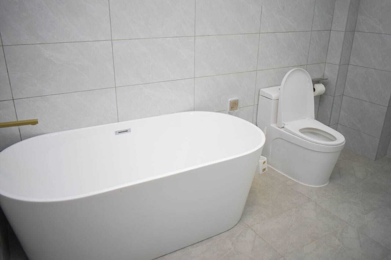 A bathroom with a white bathtub and toilet, tiled walls, and a visible electrical outlet.
