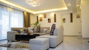 Een moderne woonkamer met een hoekbank, poufs, een salontafel en abstracte wandkunst.