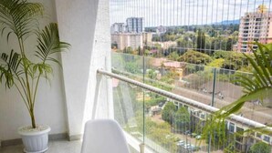 Een balkon met een ronde tafel en twee witte stoelen, een bloempot en uitzicht op een stadsbeeld.