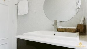 Casa de banho com lavatório branco, espelho redondo e cesto de vime.