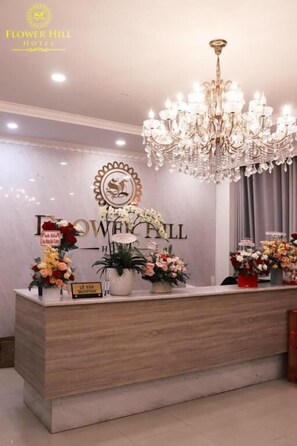 Eine Rezeption mit einem Chandelier, Blumenarrangements und einem Schild mit der Aufschrift 'Flower Hill Hotel'.