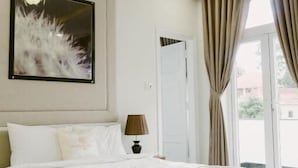 Quarto de hotel com uma cama grande, uma obra de arte emoldurada acima da cama, uma mesinha de cabeceira com uma luminária e vista pela janela.