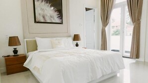Quarto de hotel com uma cama grande, duas mesas de cabeceira com luminárias, um quadro na parede e vista pela janela.