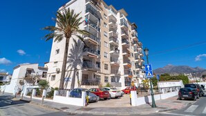 A multi-story residential building with balconies, a palm tree, and a clear blue sky.