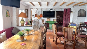 A cozy room with a wooden dining table, wicker chairs, a pool table, and a television mounted on the wall.