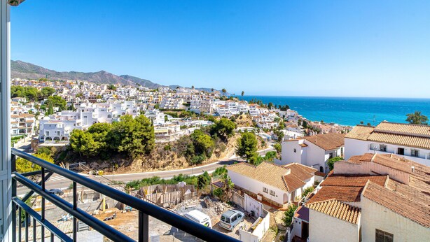 A coastal town with white buildings, a clear blue sky, and the sea in the background.