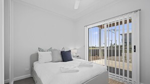 A bedroom with a bed, pillows, a nightstand, a lamp, and a view through a sliding glass door to an outdoor area. - C-Views ~ Aldinga Beach - Welcome To Your Dream Holiday House In Aldinga Beach (Aldinga Beach)
