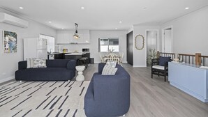 A modern living room with a sofa, a dining area with a table and chairs, and a kitchen in the background. - C-Views ~ Aldinga Beach - Welcome To Your Dream Holiday House In Aldinga Beach (Aldinga Beach)