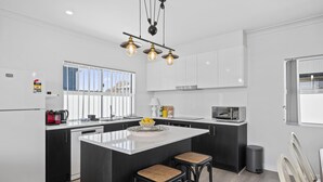 A modern kitchen with white cabinets, a central island with stools, a microwave, and a coffee maker. - C-Views ~ Aldinga Beach - Welcome To Your Dream Holiday House In Aldinga Beach (Aldinga Beach)