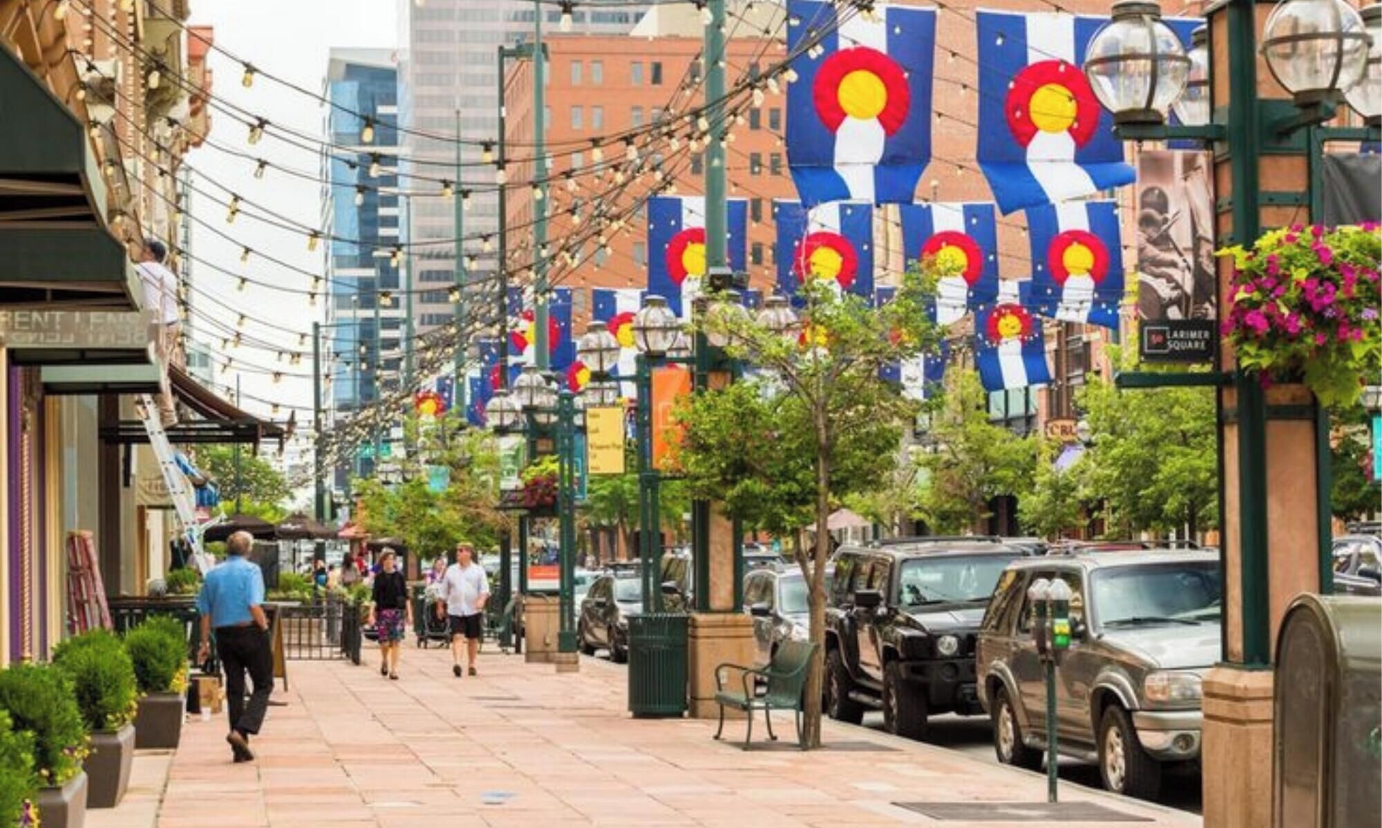 A street lined with parked cars and pedestrians walking on the sidewalk.