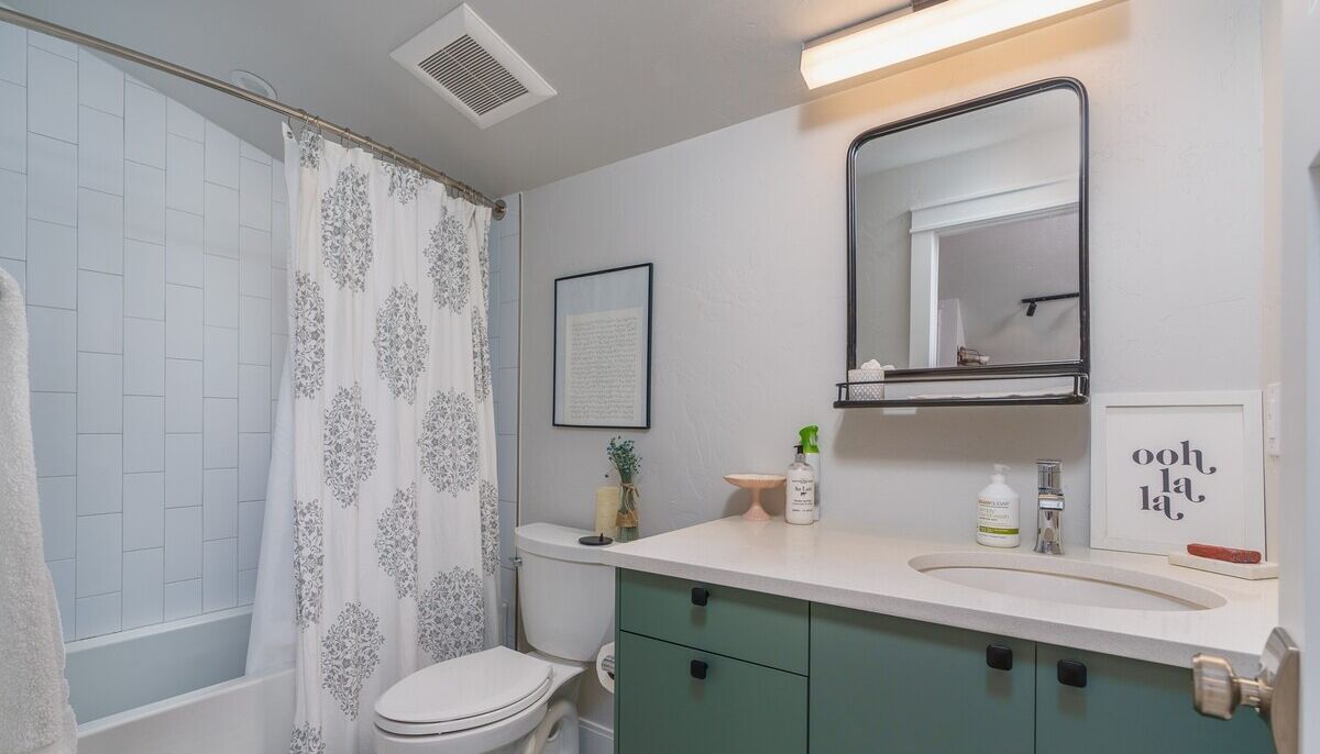 A bathroom with a shower, toilet, sink, and green cabinets.