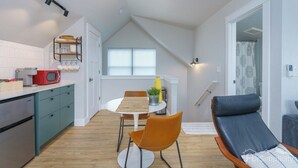 A compact kitchen with a microwave, a small dining table, and a chair. There is a sofa and a window with curtains. - Downtown Denver Guesthouse  Near RiNo (Denver)