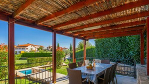 A covered outdoor dining area with a table and chairs, a pool, and a view of a residential area. - Holiday house  with pool,  garden, trampoline and a volleyball court (Vižinada)