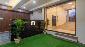 Un área de recepción con un mostrador de madera, puerta de vidrio de entrada y plantas en macetas.