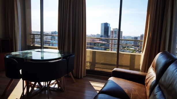 A modern living room with a glass table and leather sofa, large windows with a city view. - Charming 1-bedroom apartment in Concepción with WiFi access (Concepción)