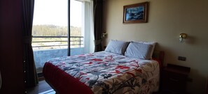 A bedroom with a large bed, a painting on the wall, and a view of a forest through the window. - Charming 1-bedroom apartment in Concepción with WiFi access (Concepción)