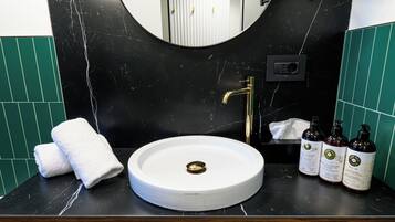 A bathroom with a round white sink, a gold faucet, and three bottles of liquid soap on the counter.