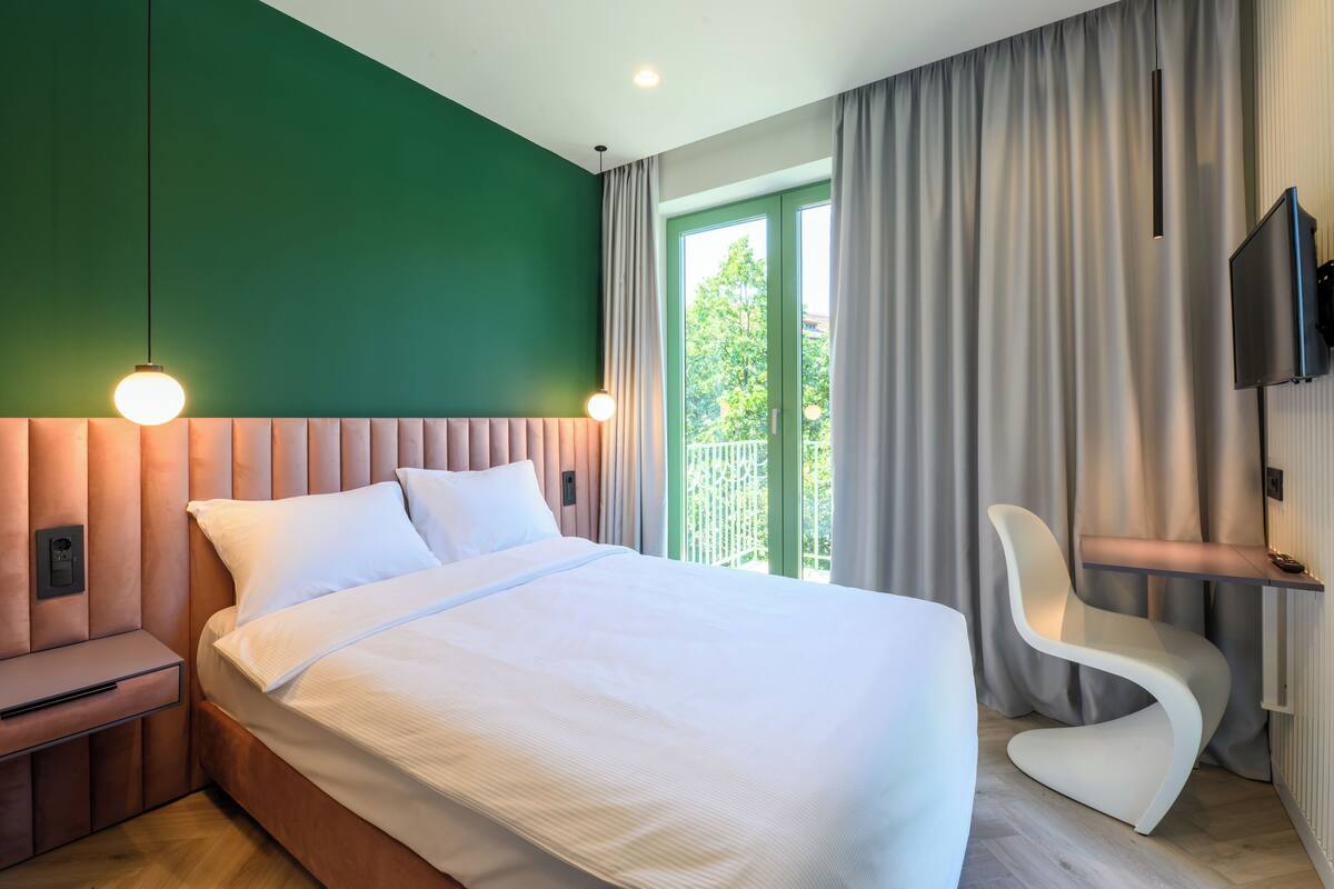 A modern hotel room with a bed, a desk, a chair, and a TV.