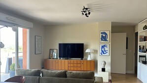 A modern living room with a sectional sofa, a flat-screen TV, a wooden cabinet, and a ceiling fan. - Top floor luxury apartment in a secure residence  (Châteauneuf-le-Rouge)